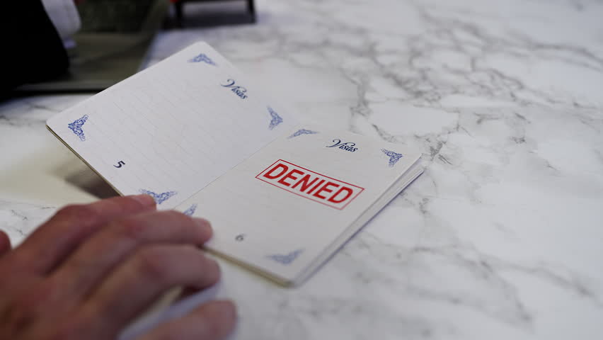 Customs officer stamps a denied seal in a UK passport, refusing person's entry