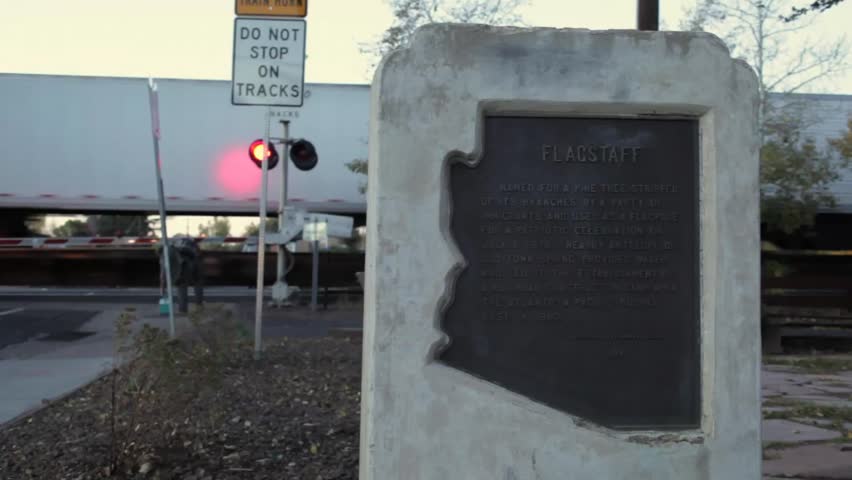 Wide angle of Flagstaff Arizona Historical Marker with railroad lights flashing and train passing by behind it.