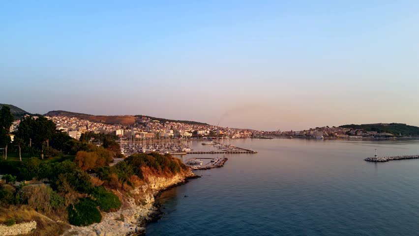 Wide aerial shot of the port of Mytilene, Lesbos, Greece, featuring boats and the glow of orange sunlight.