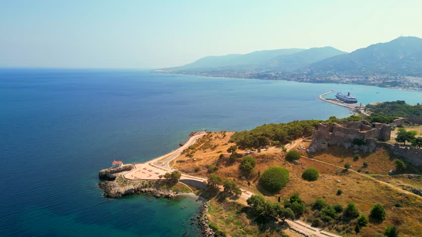 Drone shot panning across of the Castle of Mytilene, Greece, revealing a view of the port, terracotta roofed houses, and mountain hills.