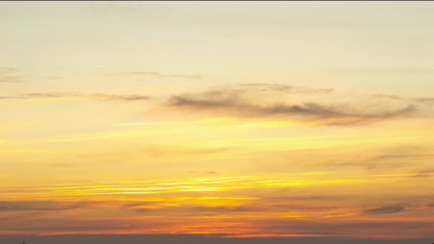 Golden sunset sky revealing fast moving clouds, creating dramatic atmospheric transition during golden hour with vibrant color gradients
