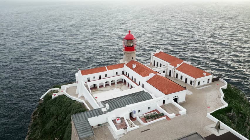 A still drone footage with smooth waves can be seen at Cabo St. Vincent Lighthouse in Sagres, Algarve Portugal.