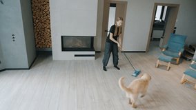 Teenage girl dancing with a mop while cleaning, as a playful Golden Retriever runs around her in a modern living room. High quality 4k footage - Powered by Shutterstock - Get 15% off with code: PIKWIZARD15