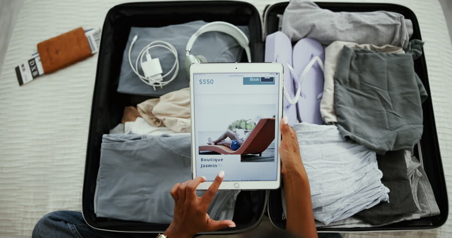 Person, hands and tablet screen for online booking with holiday, vacation or destination research in home. Woman, suitcase and browsing internet or app for travel deals and accommodation brochure