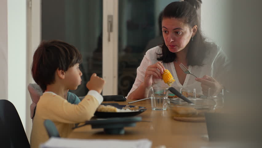 Mother and young boy sharing a conversation during family mealtime at a dining table, engaged interaction, nurturing bond, and relaxed indoor atmosphere