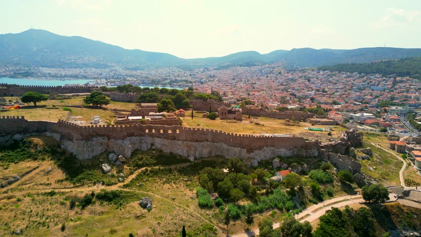 Drone shot of the Castle of Mytilene, Greece,revealing a view of the port, terracotta roofed houses, and mountain hills.