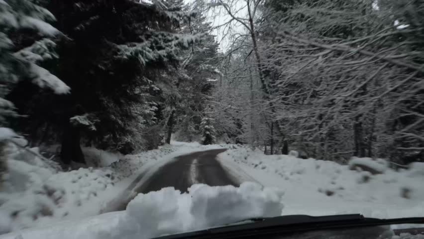 Beautiful winter drive through snow-covered forest roads. A peaceful ride with a car along winding roads in a snowy forest landscape, shot from inside the car interior.