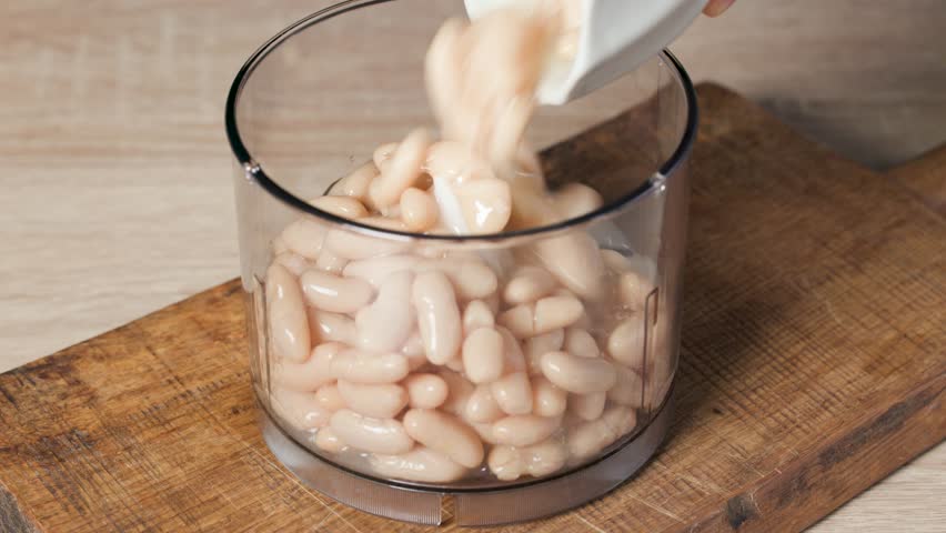 Chef is putting canned beans into a blender jar in home kitchen for making healthy mashed vegan meal, food closeup