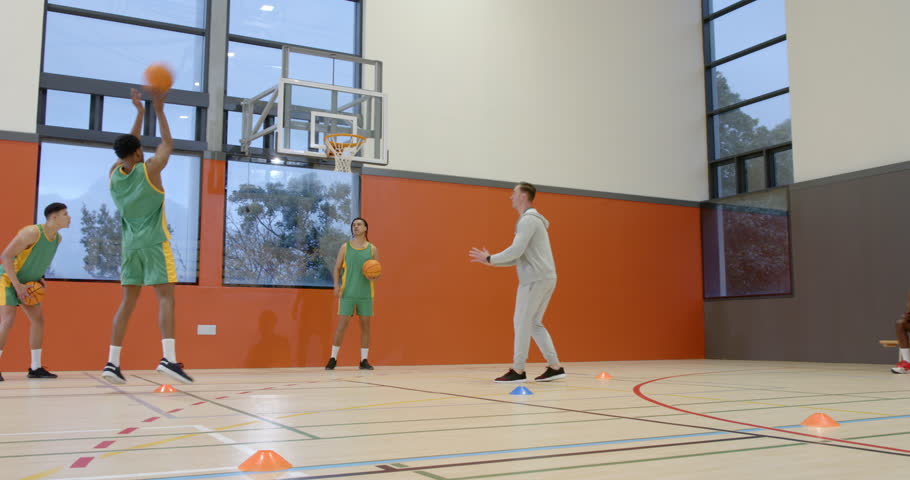 Multiracial male basketball players with coach in gym, running and throwing ball into basket. sport, lifestyle and activity.