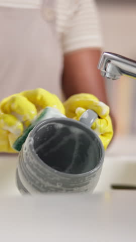 Hands, person and washing of dishes in kitchen for hygiene, bacteria safety and housekeeping routine. Cleaner, gloves and mug with chemical of cleaning service, germ protection and domestic closeup
