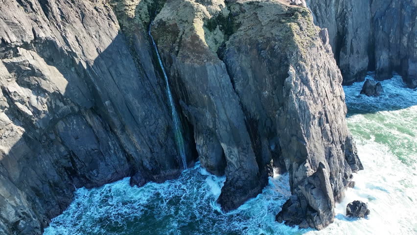 A narrow waterfall flows off a cliff into the ocean along the scenic coastline of northern Oregon. This beautiful area is accessible via highway 101 which runs along the entire west coast.