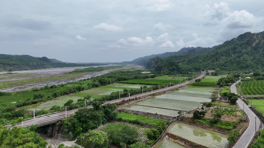 A Formosa Express 環島之星 travels thru rice paddies by Beinan River 卑南溪 on a cloudy summer day with cliffs of Liji Badlands at the foot of Mount Dulan in background, in Shanli, Beinan, Taitung, Taiwan 