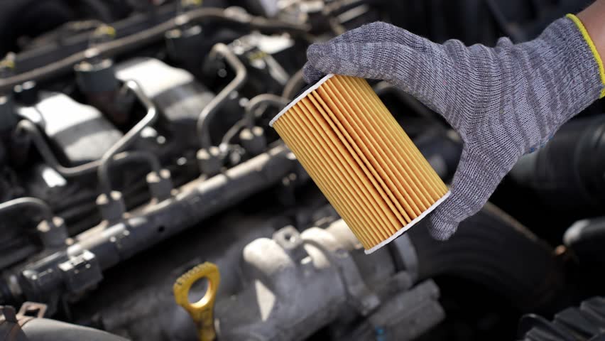 Auto mechanic holds paper oil filter for diesel cars against background of engine compartment of car. Concept of timely replacement of auto parts, replacement of oil and oil filter of car