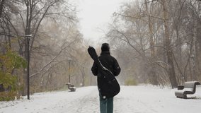 Back view of someone carrying a guitar pack while walking on a snowy path in a park, surrounded by bare winter trees and benches dusted with snow - Powered by Shutterstock - Get 15% off with code: PIKWIZARD15