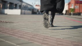 Leg view of lady in black boots and coat holding a black briefcase strolling along an interlocked path in an urban setting, depicting a business-ready stride - Powered by Shutterstock - Get 15% off with code: PIKWIZARD15