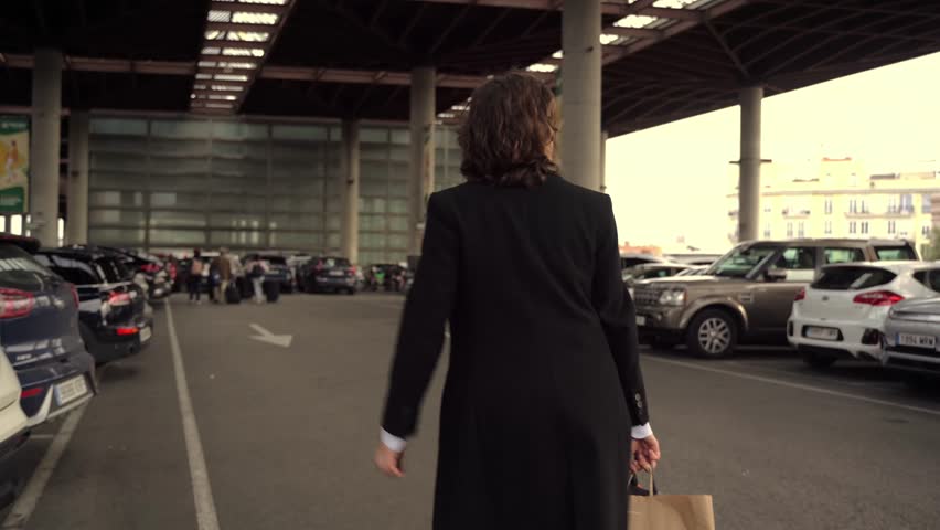 Businesswoman is walking through a parking garage while holding her car keys and a shopping bag