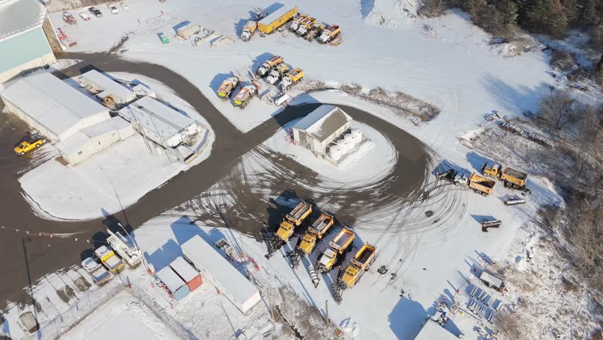 Stone industry trucks by gravel pit in snowy rural Ontario, aerial tilt up