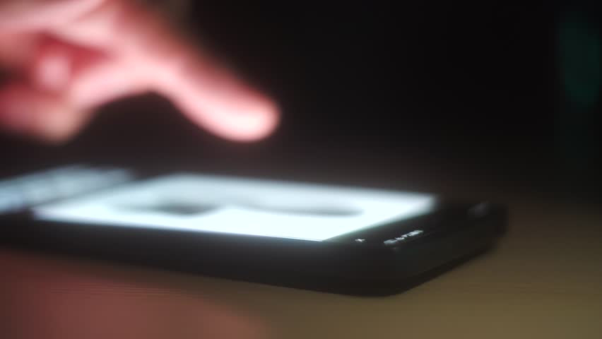 A man's finger quickly flips through the pages on the glowing screen of his smartphone In a dark room, your finger slides across the smartphone screen while scrolling through websites. 