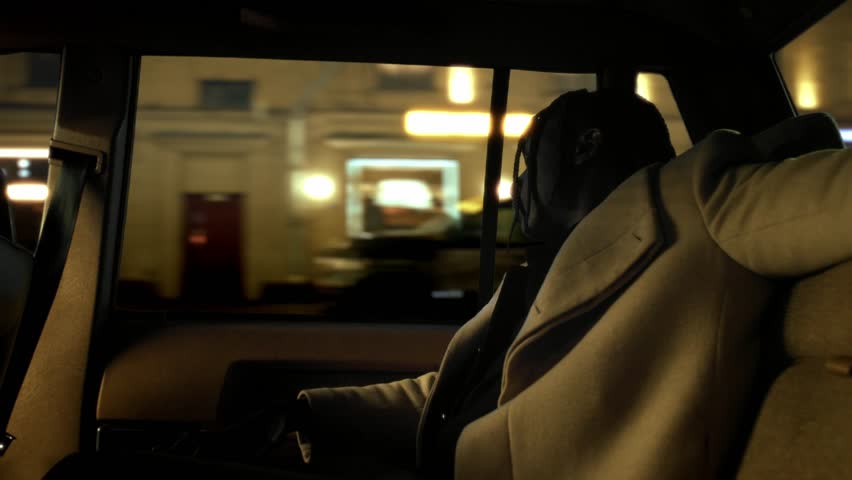 Successful black man sitting on backseat of taxi or own auto, riding at night. Rich African American male person traveling by car in city, looking at window of automobile, self-confident single man