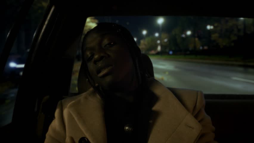 Emotional black man performing rap on back seat of auto, portrait of joyful guy . Happy African American male person riding taxi in night and flowing rap, talented charismatic musician enjoying music