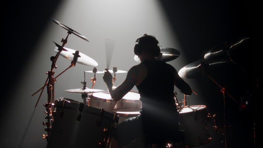 Skilled drummer punching hi-hats, playing music in rock gig, rearview in dark. Hobby and passion, young adult man rehearsing to beat rhythm, enjoy modern music, cool guy rocking crowd in concert hall