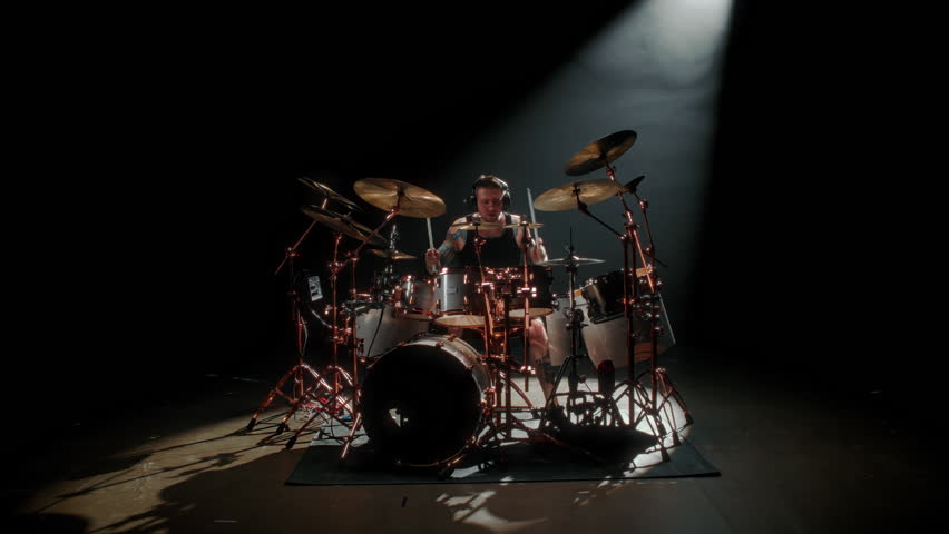 Cool drummer playing drum set in dark studio, rock band rehearsing in garage. Making music video and preparing to gig, contemporary musical style, rhythm and energy, enjoy modern music in concert hall