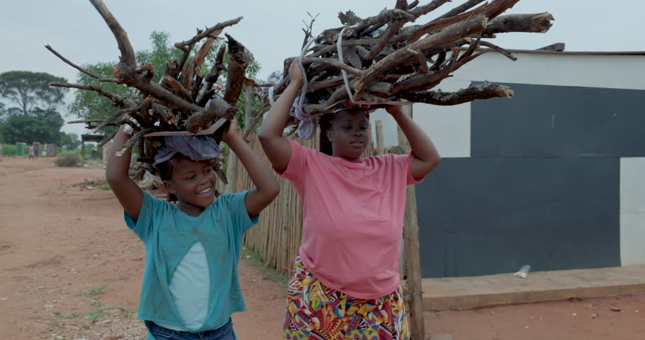 Poverty. Inequality. Close-up. Black African woman and child carrying firewood on their heads back to their shack in a township in Africa