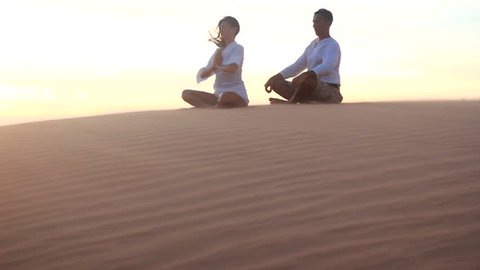 Young couple doing yoga exercises on a desert at sunrise or 