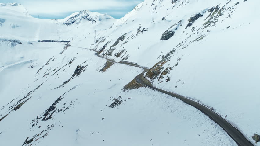 Aerial drone shot of camera fly over road high up in mountain valley leading towards mountain range in distance