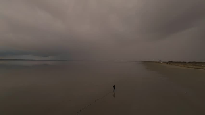 Drone orbit around a man walking on the reflective water of Tuz Lake at sunset with epic clouds