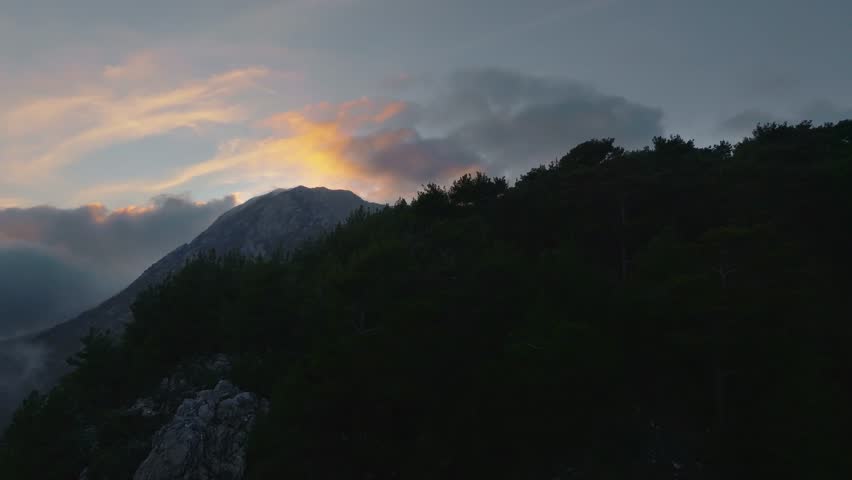 Drone view at high altitude above the clouds around the mountain at sunset