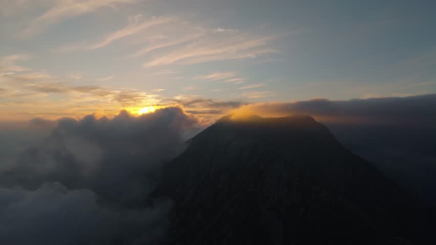 Drone view at high altitude above the clouds around the mountain at sunset
