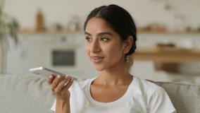 Online internet AI assistant smiling happy Indian woman Arabian female ethnic girl at home Hindu lady talking to modern voice command at mobile phone using smartphone holding gadget send audio message - Powered by Shutterstock - Get 15% off with code: PIKWIZARD15