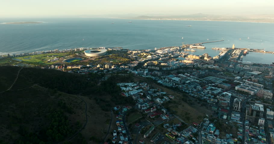 Establishing aerial view of Cape Town with Downtown, Ocean bay, Port and Landmarks. Scenic Cityscape with beautiful golden light at summer sunset. 4K shot with wide panorama from drone