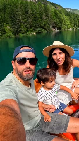 Happy family with a child taking a selfie while enjoying a boat trip on the beautiful lake braies in the dolomites, italy, during summer