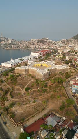 Vertical aerial shot with lateral movement over the Fort of San Diego in Acapulco, highlighting its surroundings.