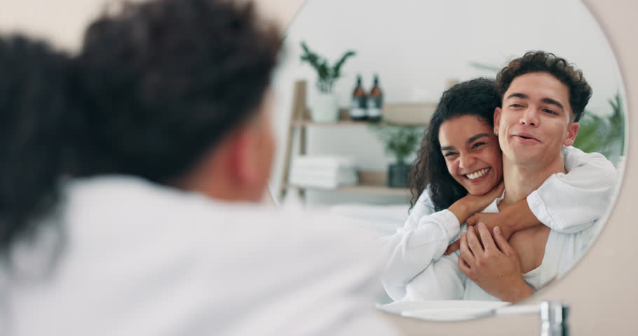 Home, mirror and happy couple hug for love, care or support in healthy relationship. Reflection, man and woman embrace together in bathroom for romance, morning routine and skincare for facial beauty