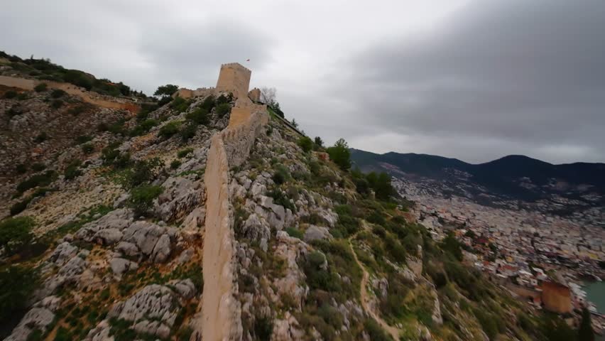 FPV drone ascent closely along the wall of Alanya Fortress, passing near the tower with the Turkish flag