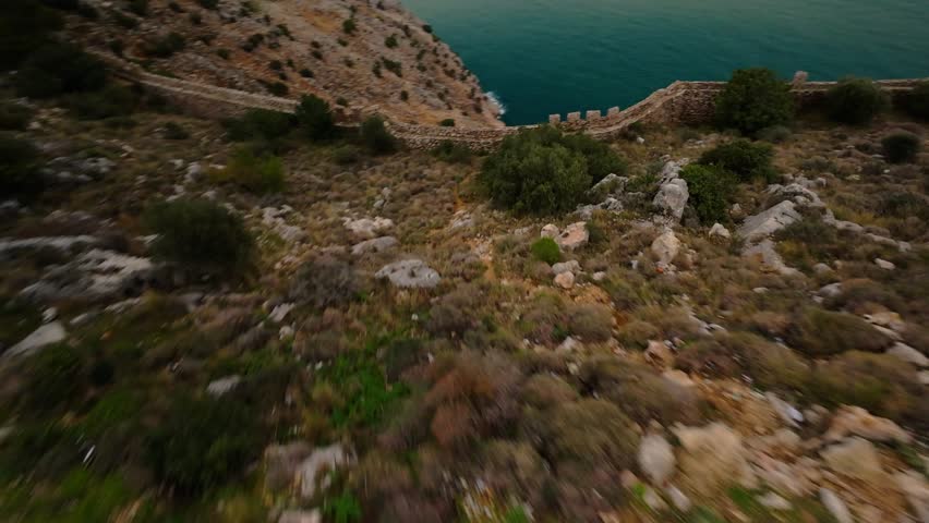 Dynamic FPV drone flight over the Alanya fortress wall above the Mediterranean Sea in cloudy weather with soft light