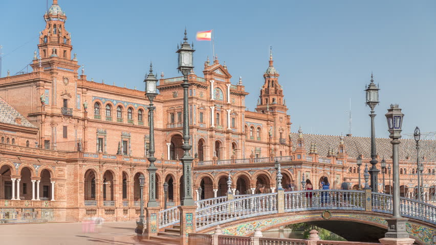 Plaza de Espana in Seville timelapse hyperlapse, a grand architectural complex in Maria Luisa Park built for the Ibero-American Exposition. Bridges, canal and vintage streetlights under blue sky.