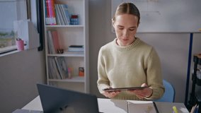 Focused teacher using tablet at school workplace closeup. Calm serious woman working at class room preparing to online lesson. Attentive educator checking homework using pad computer at cabinet alone - Powered by Shutterstock - Get 15% off with code: PIKWIZARD15