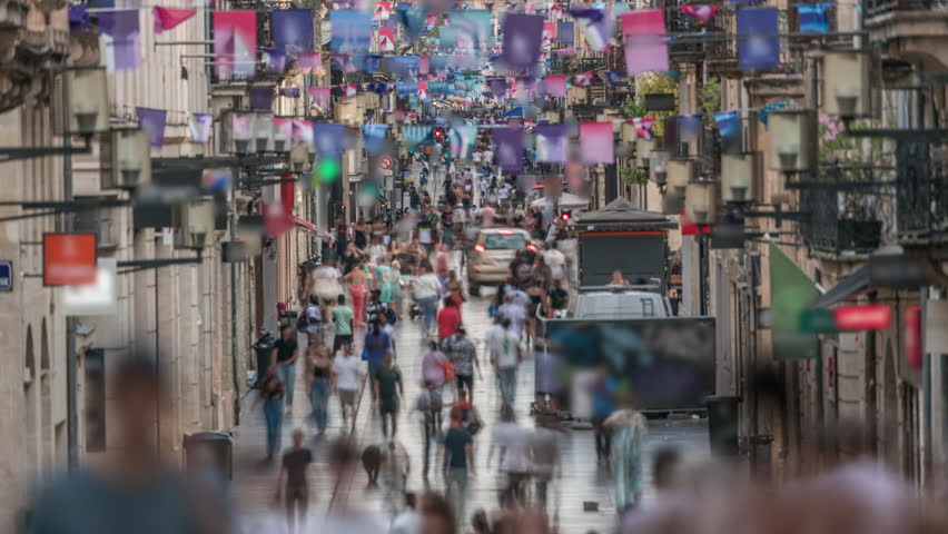 Tourists and locals walking and shopping in Rue Sainte-Catherine timelapse, Bordeaux, France. The longest pedestrian street in the country. Atmosphere of urban life. Colorful flags decorate the street