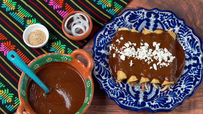Mexican woman prepares chicken mole enchiladas, spreading crumbled cheese on a plate with enmoladas