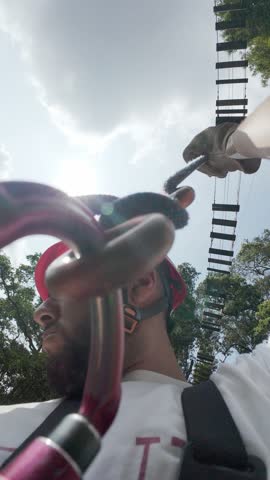 Bold man wearing helmet and doing rappel down from a suspension bridge with some safety gear and strings