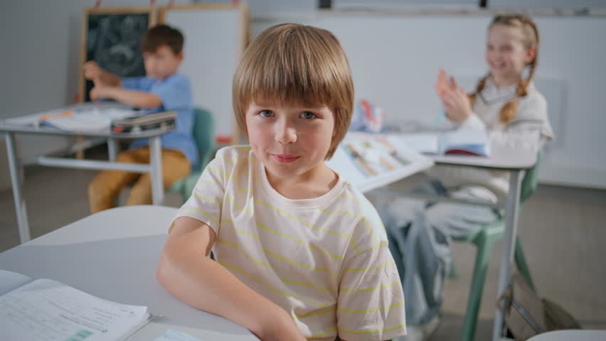 Happy boy raising hand at lesson closeup. Smiling pupil listening teacher answering question at school room portrait. Smart child enjoying class work. Small clever schoolboy learning in classroom