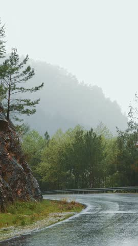 Empty mountain road at rainy day. Mountain peaks with green trees forest at rain. Amazing mountain landscape nature. Vertical video