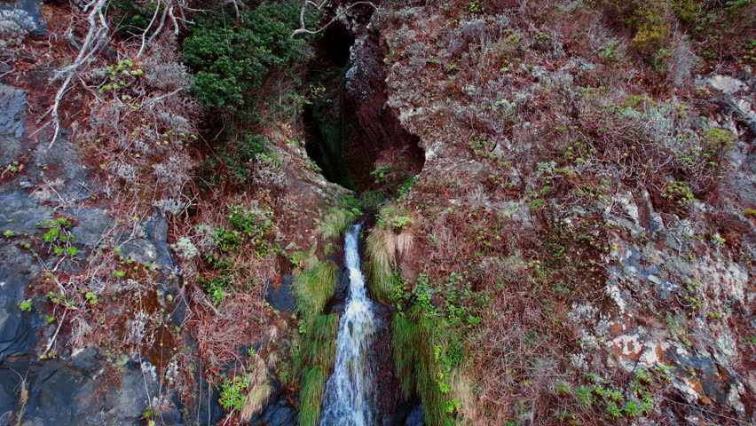 Chasm among the huge rocks and water flowing from it. Drone footage distancing from a waterfall that lands at the highway. Madeira, Portugal.