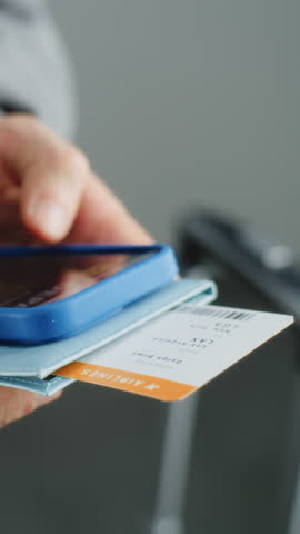 Airport Terminal: Close Up of Man Holding Documents with Ticket in Hands, Checking Flight Information Using Smartphone, Surfing the Internet or Social Networks. Traveler Going on Trip. Vertical Shot.