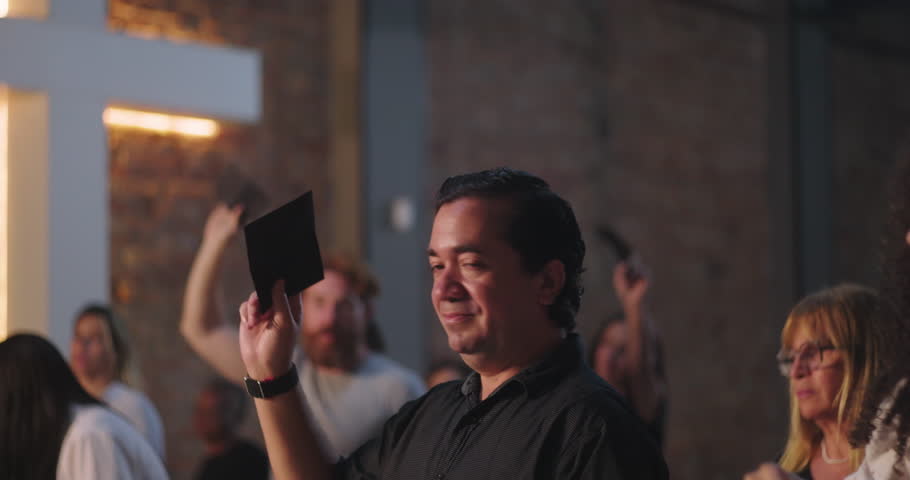 Man of Hispanic descent holding offering envelope inside church, communal gathering, spiritual moment, worship service, focus on individual, group celebration in religious space