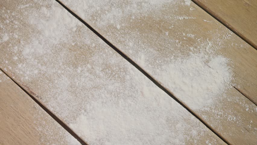 Large, soft, round white dough, raised by yeast, is thrown onto wooden table sprinkled with flour. Then woman